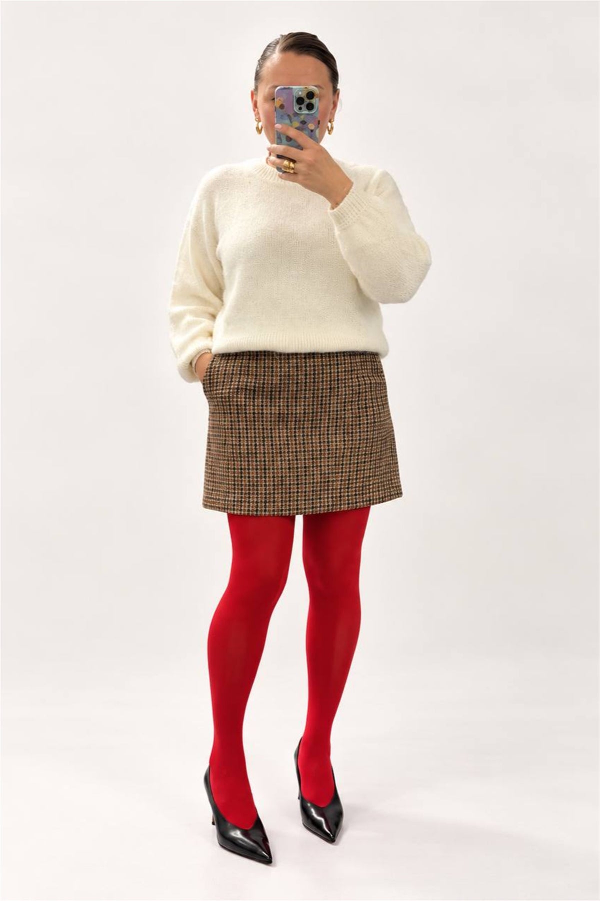 Minigonna a quadretti marroni indossata con maglione panna e collant rossi, vista frontale